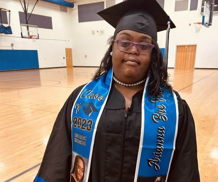 Female student with Down syndrome poses in graduation cap and gown.